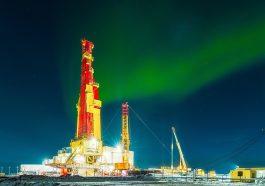 A brightly lit oil drilling rig under an aurora-filled night sky.